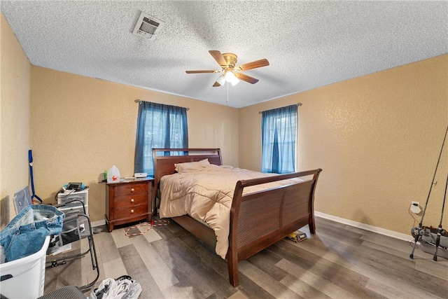 bedroom featuring wood finished floors, visible vents, a textured wall, and baseboards