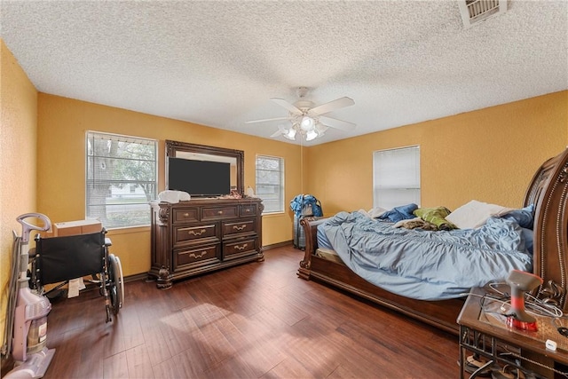 bedroom with a ceiling fan, dark wood-style floors, visible vents, a textured ceiling, and a textured wall