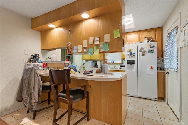 kitchen featuring a peninsula, white refrigerator with ice dispenser, light countertops, and a textured ceiling