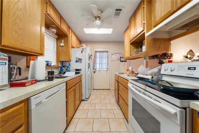 kitchen featuring visible vents, ceiling fan, light countertops, a skylight, and white appliances