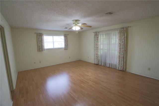 empty room with ceiling fan, light wood-type flooring, and a textured ceiling