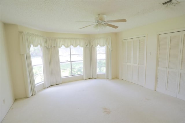 empty room with ceiling fan, light colored carpet, and a textured ceiling