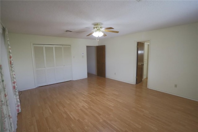 unfurnished bedroom with ceiling fan, light wood-type flooring, a textured ceiling, and a closet