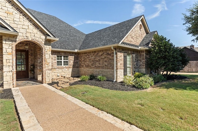 doorway to property with brick siding, stone siding, a shingled roof, and a yard