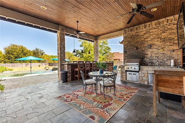 view of patio / terrace featuring exterior kitchen, outdoor dining area, a fenced backyard, area for grilling, and a ceiling fan