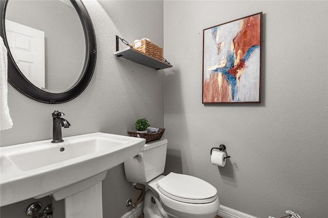 bathroom with baseboards, toilet, and a textured wall