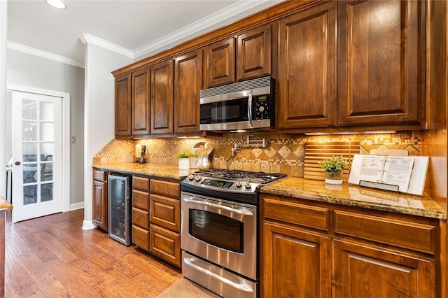 kitchen with crown molding, light stone countertops, beverage cooler, appliances with stainless steel finishes, and wood finished floors