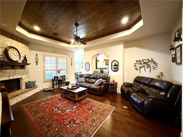 living room with dark hardwood / wood-style flooring, a stone fireplace, wooden ceiling, and a raised ceiling