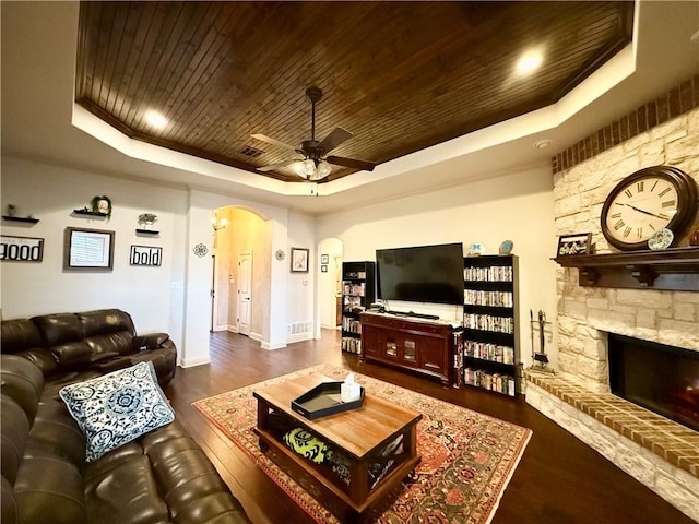 living room with dark hardwood / wood-style flooring, wood ceiling, a stone fireplace, and a raised ceiling