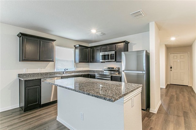 kitchen featuring sink, a center island, dark wood-type flooring, dark stone countertops, and appliances with stainless steel finishes