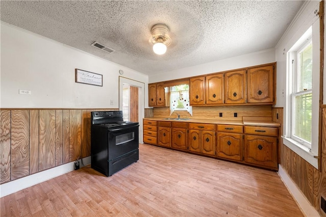 kitchen with black range with electric stovetop, sink, wooden walls, a textured ceiling, and light hardwood / wood-style floors