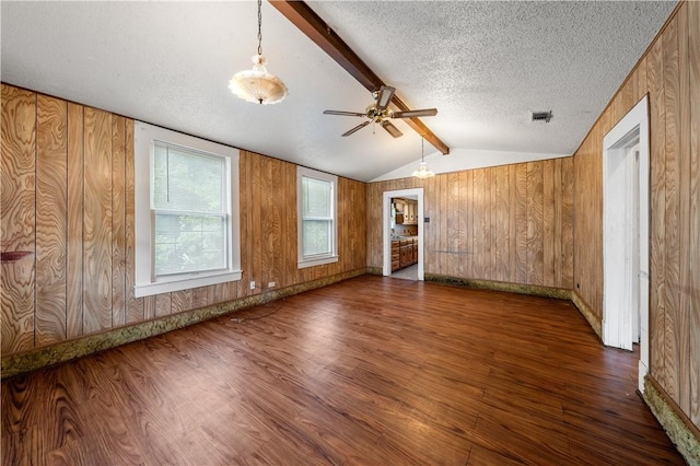 empty room with wood walls, lofted ceiling with beams, ceiling fan, a textured ceiling, and dark hardwood / wood-style flooring