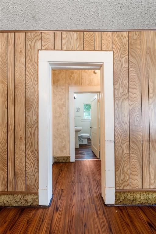 corridor featuring wood walls, dark wood-type flooring, and a textured ceiling