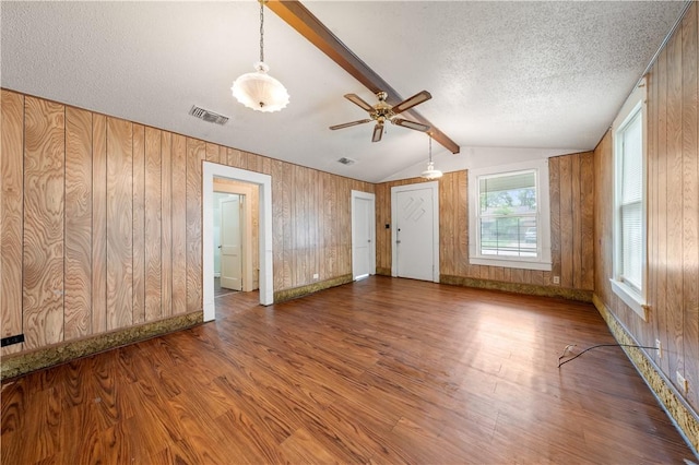 empty room with lofted ceiling with beams, wooden walls, wood-type flooring, and a textured ceiling