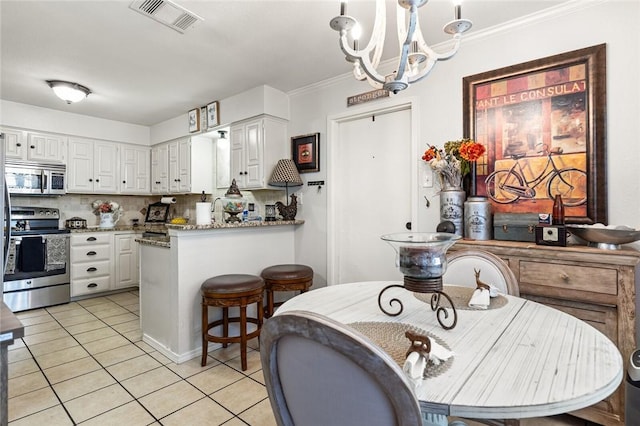 kitchen featuring decorative backsplash, appliances with stainless steel finishes, an inviting chandelier, white cabinets, and light tile patterned flooring