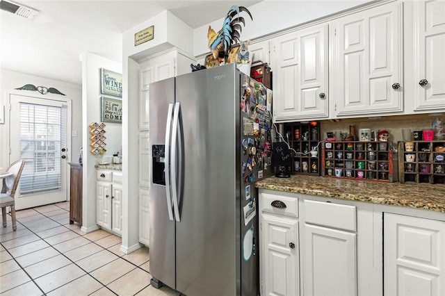 kitchen featuring stainless steel refrigerator with ice dispenser, ornamental molding, dark stone countertops, white cabinetry, and light tile patterned flooring