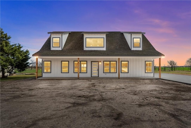 back of house at dusk featuring board and batten siding and roof with shingles