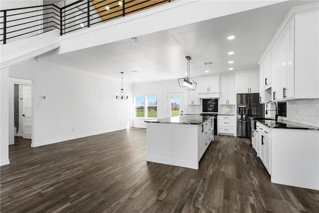 kitchen with a center island, dark wood-type flooring, decorative backsplash, black fridge, and white cabinets