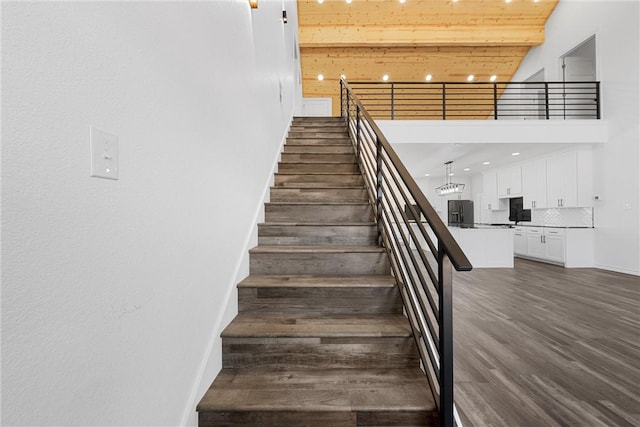 stairs featuring wood finished floors, baseboards, beam ceiling, a high ceiling, and wood ceiling