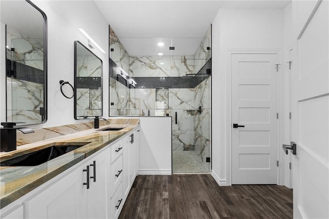 full bath with a sink, a marble finish shower, wood finished floors, and double vanity