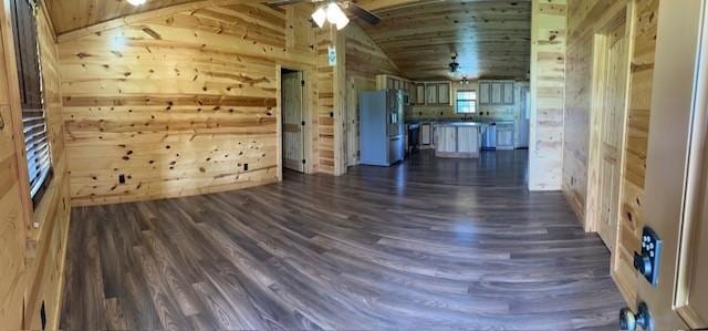 unfurnished living room featuring ceiling fan, dark wood-type flooring, and wooden walls