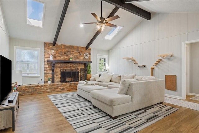 living room featuring a fireplace, vaulted ceiling with skylight, wood finished floors, and ceiling fan