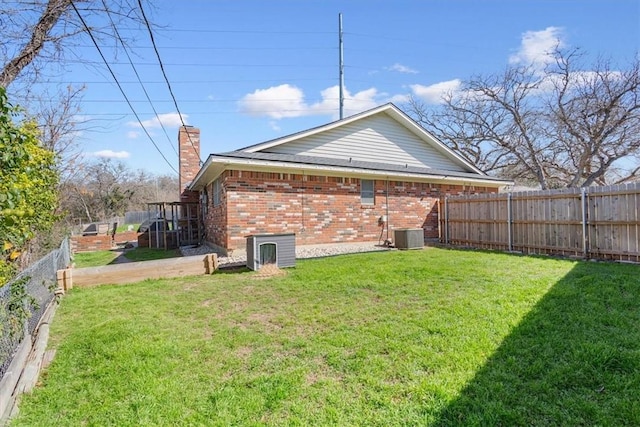 rear view of house featuring central air condition unit, a lawn, a fenced backyard, brick siding, and a chimney