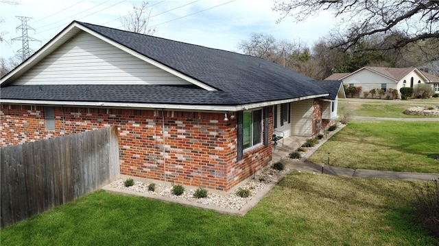 view of side of property with brick siding, roof with shingles, a lawn, and fence