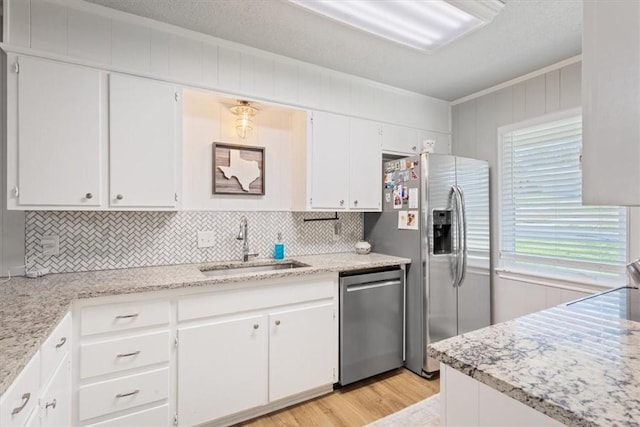 kitchen with light wood-style flooring, a sink, appliances with stainless steel finishes, white cabinets, and crown molding