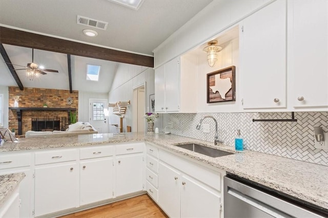 kitchen featuring visible vents, backsplash, dishwasher, vaulted ceiling with skylight, and a sink