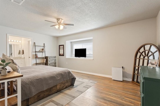 bedroom featuring visible vents, a textured ceiling, ensuite bath, wood finished floors, and baseboards