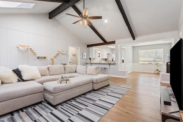 living area with vaulted ceiling with skylight, a ceiling fan, and light wood finished floors