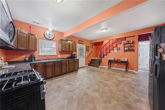 kitchen with black fridge, white gas range, a textured ceiling, sink, and beam ceiling