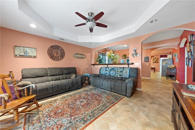 living room with a raised ceiling and ceiling fan