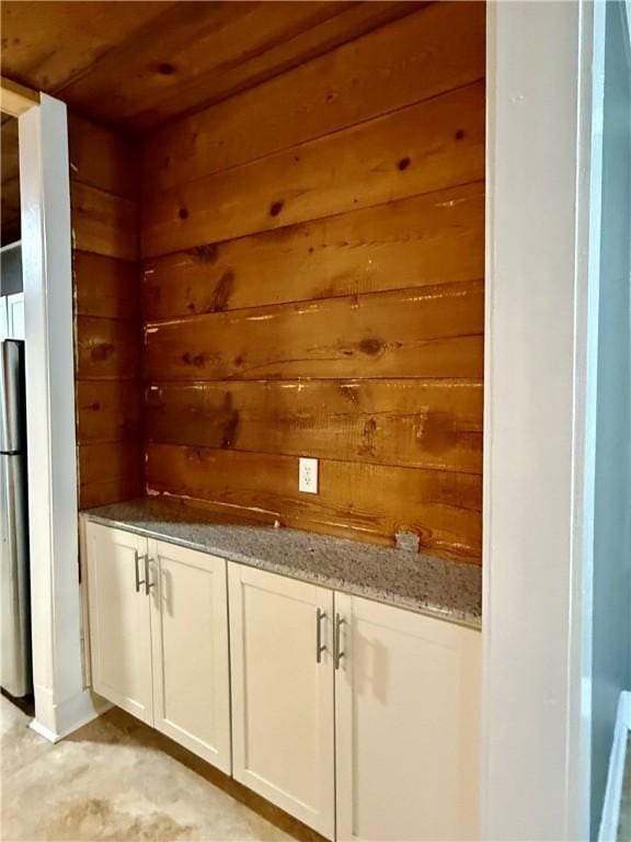 interior space featuring wood walls, stainless steel fridge, white cabinets, wood ceiling, and light stone countertops