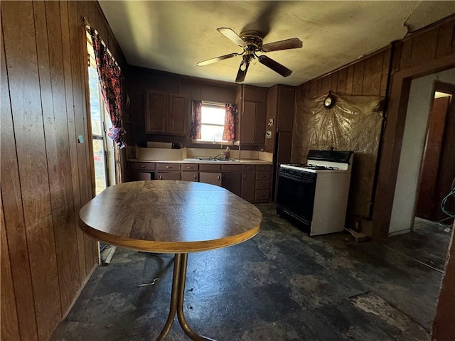 kitchen featuring ceiling fan, sink, white range with gas stovetop, and wood walls