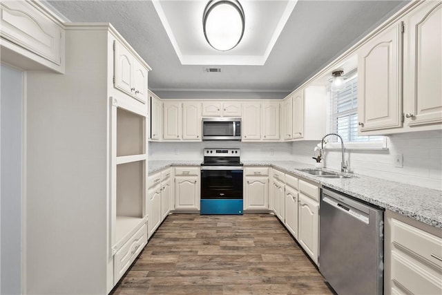 kitchen with white cabinetry, sink, light stone countertops, a raised ceiling, and appliances with stainless steel finishes