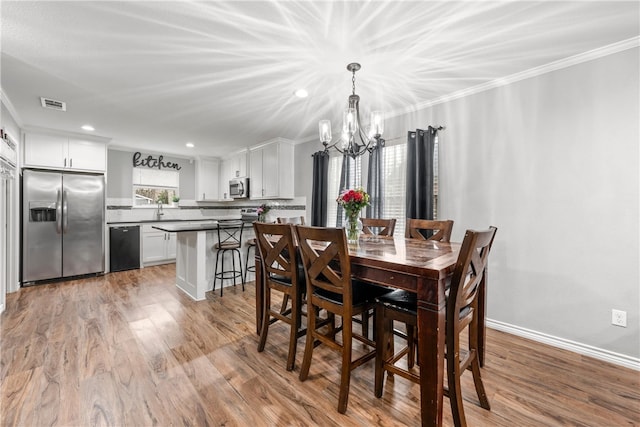 dining space featuring sink, ornamental molding, a chandelier, and light hardwood / wood-style flooring