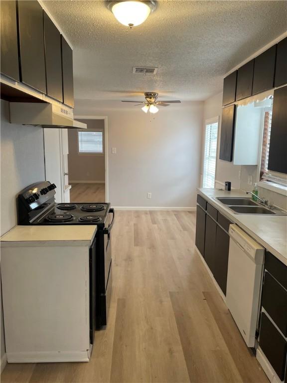 kitchen featuring white dishwasher, sink, light hardwood / wood-style flooring, black electric range, and a textured ceiling