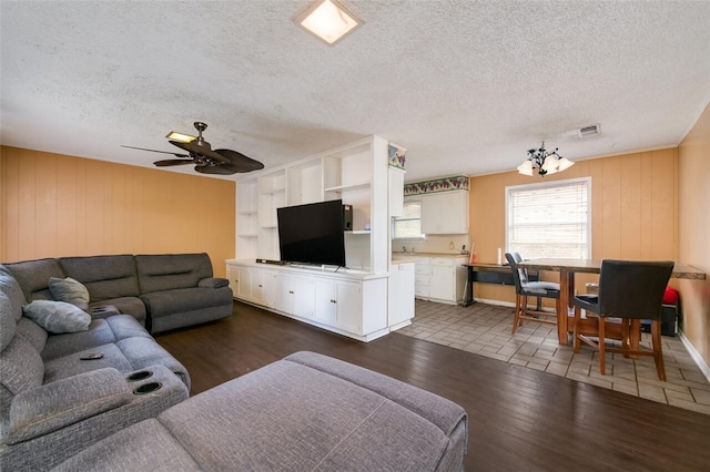 living room featuring ceiling fan with notable chandelier, dark hardwood / wood-style flooring, a textured ceiling, and wooden walls