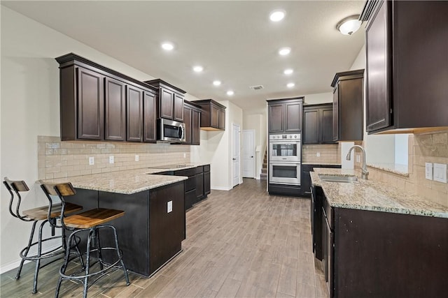 kitchen with appliances with stainless steel finishes, backsplash, light stone counters, sink, and light hardwood / wood-style floors