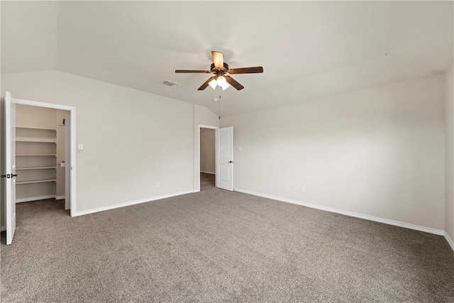 unfurnished bedroom featuring ceiling fan, a spacious closet, lofted ceiling, a closet, and dark carpet