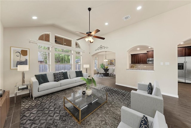 living room featuring sink, high vaulted ceiling, dark wood-type flooring, and ceiling fan with notable chandelier