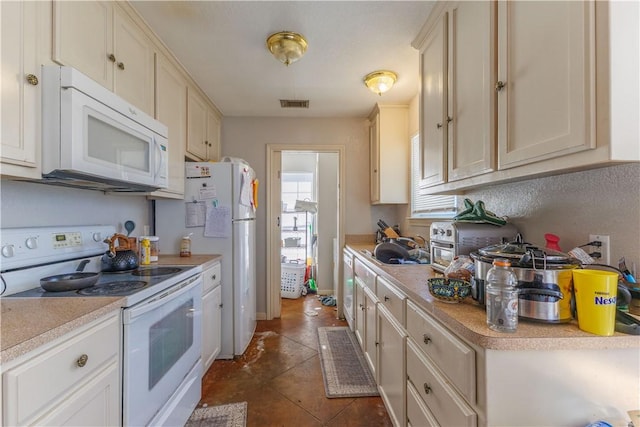 kitchen with white appliances, dark tile patterned flooring, a sink, visible vents, and light countertops