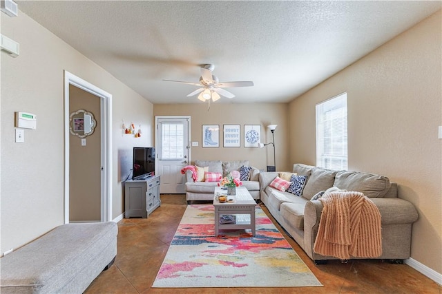 living area with tile patterned flooring, ceiling fan, baseboards, and a textured ceiling