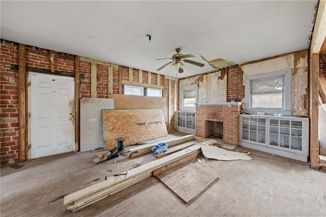 unfurnished living room with brick wall, plenty of natural light, ceiling fan, and a brick fireplace