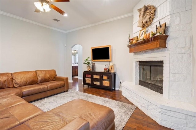 living room with arched walkways, a large fireplace, crown molding, and wood finished floors