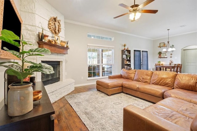 living room with a large fireplace, ceiling fan with notable chandelier, crown molding, and wood finished floors