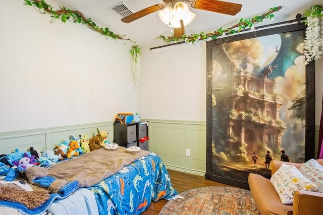 bedroom featuring visible vents, wood finished floors, wainscoting, and a decorative wall