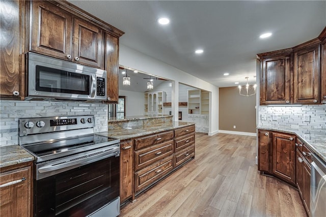 kitchen featuring light wood-type flooring, backsplash, light stone counters, stainless steel appliances, and a chandelier